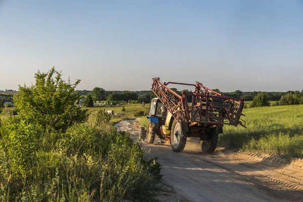 Egy kék traktor-pótkocsi mezőgazdasági munkák túrák végig az út a búza mező. — Stock Fotó