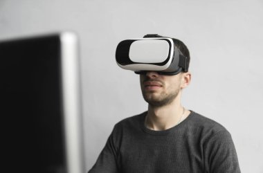 Sanal gerçeklik giyen genç adam kulaklık, vr kutusu ve bilgisayar monitörü karşı ofiste oturan gözlükler. Bağlantı, teknoloji, yeni nesil, ilerleme kavramı.