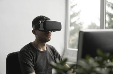 Sanal gerçeklik giyen genç adam kulaklık, vr kutusu ve bilgisayar monitörü karşı ofiste oturan gözlükler. Bağlantı, teknoloji, yeni nesil, ilerleme kavramı.