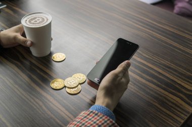 Zengin bir bitcoin para tutan ve bir masaya bitcoin telefon ve altın sikkeleri ile bir kahve içme dostum. Bitcoins incelemesi üzerinden kar.