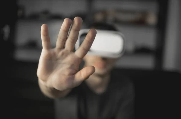 Giovane uomo barbuto che indossa cuffie della realtà virtuale in ufficio seduto su un divano e cercando di toccare qualcosa che vede nel mondo virtuale . — Foto Stock