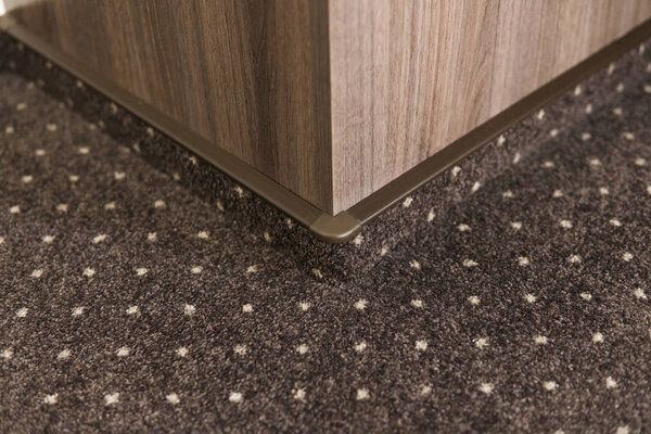 Brown carpet floor with a white dots with a carpet baseboard on a wood-based panels wall.