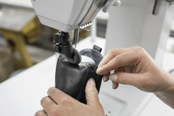 Швейная машина в кожаной мастерской в действии с руками, работающими над кожаными деталями для обуви. Руки пожилых женщин с швейной машинкой на обувной фабрике . — стоковое фото