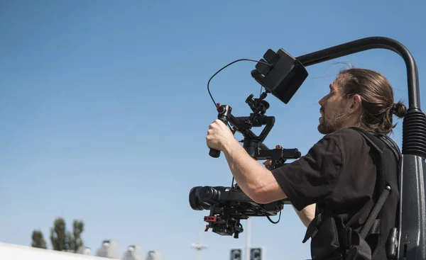 Professionell filmare håller kameran på 3-axlig gimbal som monterade på lätt rigg. Filmare använda steadicam. Pro utrustning hjälper till att göra högkvalitativa video utan skakningar. — Stockfoto