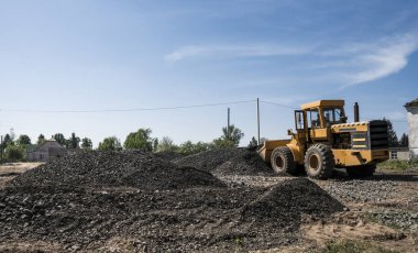 Sarı yükleyici boş kova ile bir taş çakıl yol inşaat çalışmaları sırasında duruyor. Yolun taşları. Boşaltma taş