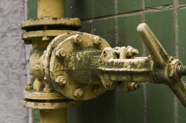 Eski gaz vinç ve boru yeşil duvar arka plan üzerinde yıpranmış. Eski gaz kapı sarı renkteki bir boru ve boru engeller. Boru hattı ile duvara vererek gaz için Vinçler.