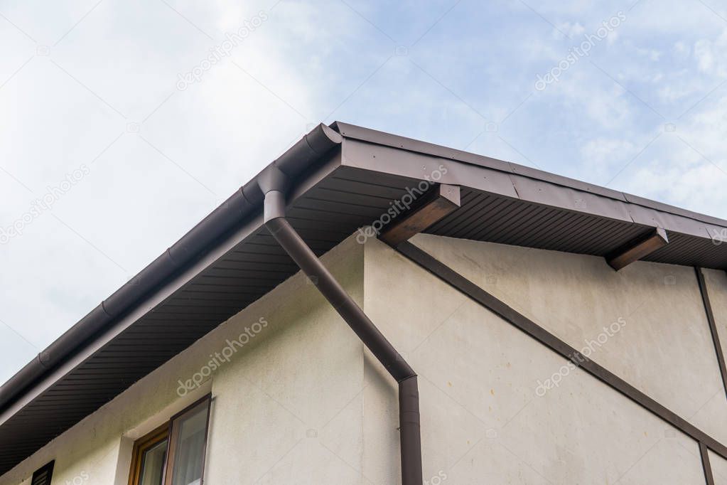 Modern roof covered with tile effect PVC coated brown metal roof sheets against cloudy sky.