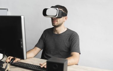 Sanal gerçeklik giyen genç adam kulaklık, vr kutusu ve bilgisayar monitörü karşı ofiste oturan gözlükler. Bağlantı, teknoloji, yeni nesil, ilerleme kavramı.