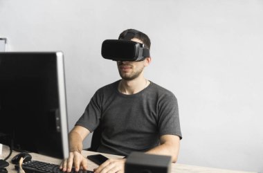 Sanal gerçeklik giyen genç adam kulaklık, vr kutusu ve bilgisayar monitörü karşı ofiste oturan gözlükler. Bağlantı, teknoloji, yeni nesil, ilerleme kavramı.