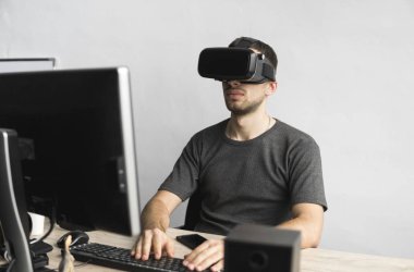 Sanal gerçeklik giyen genç adam kulaklık, vr kutusu ve bilgisayar monitörü karşı ofiste oturan gözlükler. Bağlantı, teknoloji, yeni nesil, ilerleme kavramı.
