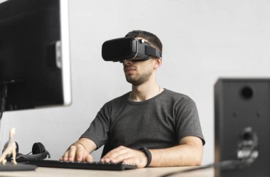 Sanal gerçeklik giyen genç adam kulaklık, vr kutusu ve bilgisayar monitörü karşı ofiste oturan gözlükler. Bağlantı, teknoloji, yeni nesil, ilerleme kavramı.