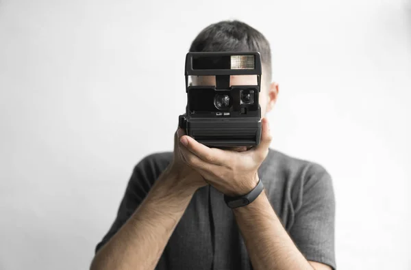 Pohledný mladý vousatý muž v černé košili drží fotoaparát vintage staromódní film na bílém pozadí a při pohledu do fotoaparát hledáček. — Stock fotografie
