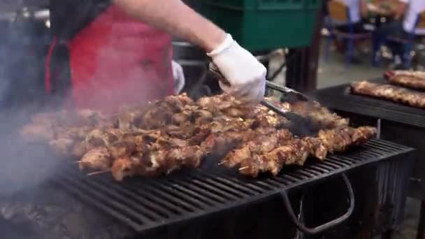 Mand madlavning kød på grill grill til sine venner på sommer udendørs fest. Madlavning svinekød på varmt kul. Nærbillede af traditionel picnic parabol. Grillkød på trækul . – Stock-video