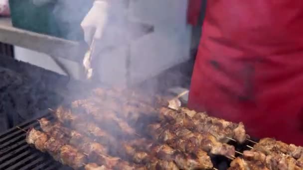 夏の屋外パーティーで彼の友人のためのバーベキューグリルで肉を調理する男。豚肉を熱炭で調理する。伝統的なピクニック料理のクローズアップ。木材石炭で肉を焼く. — ストック動画