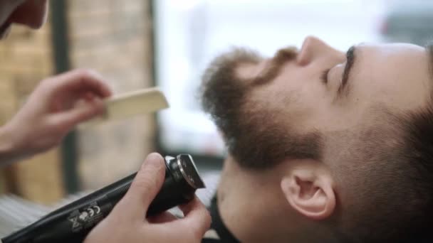 A arrumar a barba. Barbearia. Homem cabeleireiro fazendo barba de corte de cabelo homens adultos no salão de cabeleireiro dos homens com um cortador elétrico. Um jovem bonito a cortar a barba na barbearia . — Vídeo de Stock