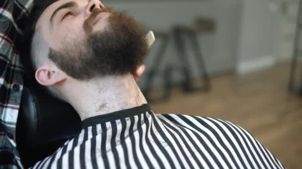 Grooming the beard. Barbershop. Man hairdresser doing haircut beard adult men in the mens hair salon with a electric clipper. Handsome young man getting his beard cut at the barbershop. — Stock Video