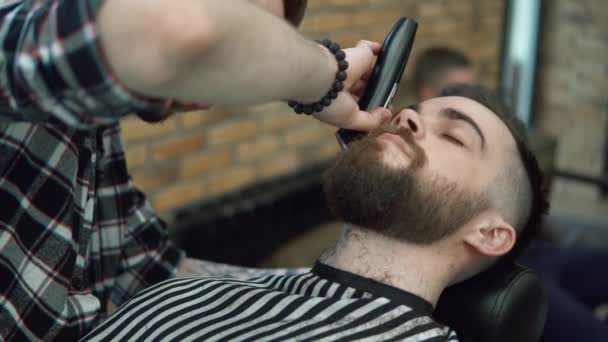 A arrumar a barba. Barbearia. Homem cabeleireiro fazendo barba de corte de cabelo homens adultos no salão de cabeleireiro dos homens com um cortador elétrico. Um jovem bonito a cortar a barba na barbearia . — Vídeo de Stock