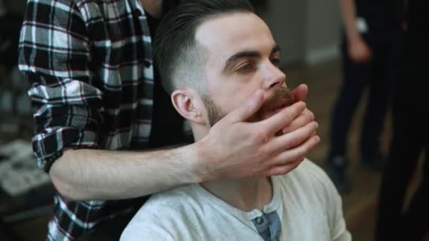 Close-up de barbeiro fazendo styling com um homem bonito com uma longa barba. Cabeleireiros mãos no processo de trabalho. Barbeiro fazendo corte de cabelo de homem barbudo atraente na barbearia. Cabeleireiro no trabalho . — Vídeo de Stock