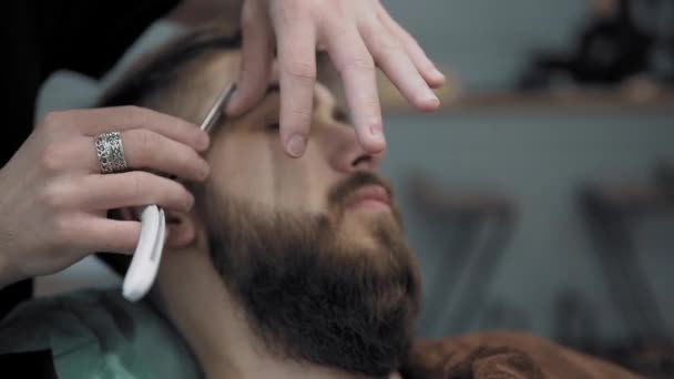 Peluquero afeita a los hombres con una barba larga con hoja de afeitar recta en s peluquería o barbería. Mans corte de pelo y afeitado en la peluquería, peluquería y salón de afeitar . — Vídeos de Stock