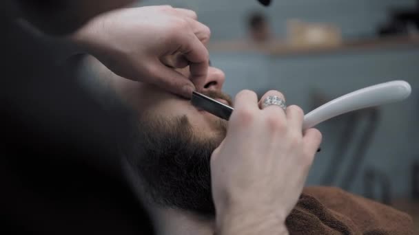 Peluquero afeita a los hombres con una barba larga con hoja de afeitar recta en s peluquería o barbería. Mans corte de pelo y afeitado en la peluquería, peluquería y salón de afeitar . — Vídeos de Stock