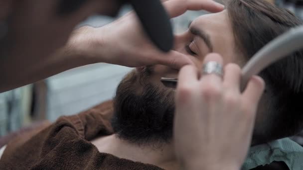Peluquero afeita a los hombres con una barba larga con hoja de afeitar recta en s peluquería o barbería. Mans corte de pelo y afeitado en la peluquería, peluquería y salón de afeitar . — Vídeos de Stock