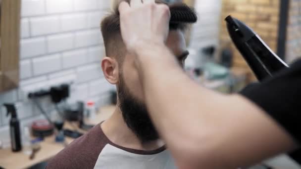 Primer plano de peluquero haciendo estilo con un hombre guapo con una barba larga. Peluqueros manos en el proceso de trabajo. Peluquero haciendo corte de pelo de hombre barbudo atractivo en la barbería. Peluquería en el trabajo . — Vídeos de Stock