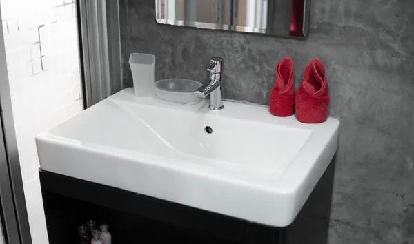 Современный кран из нержавеющей стали с умывальником с двумя красными полотенцами на нем. Интерьер в ванной комнате современный. Роскошная и стильная ванная комната с бетонными стенами . — стоковое фото