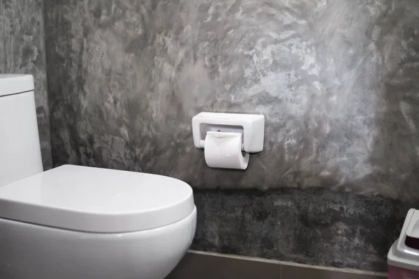 Vit hängande toalettsits på vit toalett i hemmet badrum med grå kakel i betong stil och toalettpapper på väggen. Badrum lyx interiör. — Stockfoto