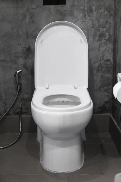 Witte hangende wc-bril op wit toilet in het huis badkamer met grijze tegels in beton stijl en wc-papier aan de muur. Badkamer luxe interieur. — Stockfoto