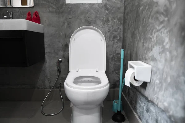 Fehér lógó WC-ülőke a fehér WC-ben az otthoni fürdőszobában szürke csempe beton stílusban és WC-papír a falon. Fürdőszoba luxusbelső. — Stock Fotó