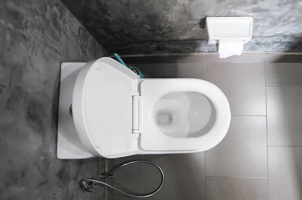 Siège de toilette suspendu blanc sur des toilettes blanches dans la salle de bain à la maison avec des carreaux gris en béton et du papier toilette sur le mur. Salle de bain luxe intérieur . — Photo