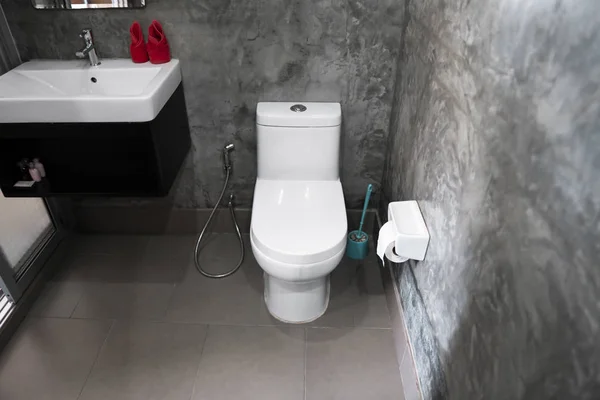 Weißer hängender Toilettensitz auf weißer Toilette im heimischen Badezimmer mit grauen Fliesen im Betonstil und Toilettenpapier an der Wand. Badezimmer Luxus Interieur. — Stockfoto