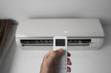 Uzaktan kumanda kullanan adam eli. Beyaz bir duvara monte edilmiş klimanın el tutma rc ve ayar sıcaklığı. Indooor konfor sıcaklığı. Sağlık kavramları ve enerji tasarrufu.