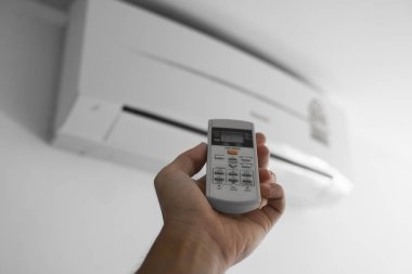 Uzaktan kumanda kullanan adam eli. Beyaz bir duvara monte edilmiş klimanın el tutma rc ve ayar sıcaklığı. Indooor konfor sıcaklığı. Sağlık kavramları ve enerji tasarrufu.