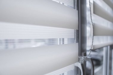 Oturma odasında beyaz plastik pencereüzerinde beyaz kumaş rulo jaluman detayları. Rulo perdeleri kapalı kapatın.