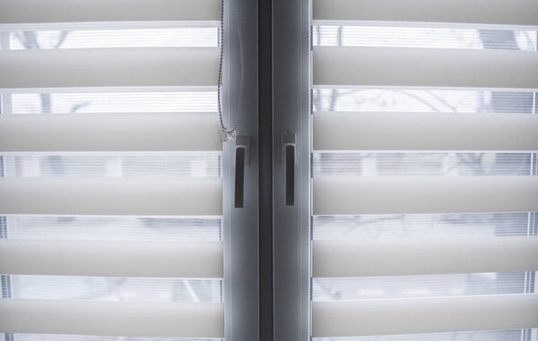 White fabric roller blinds on the white plastic window in the living room. Roll curtains indoor.