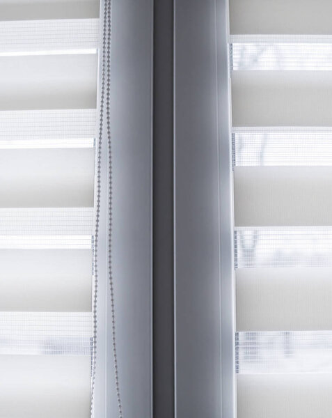 Details of white fabric roller blinds on the white plastic window in the living room. Close up on roll curtains indoor.