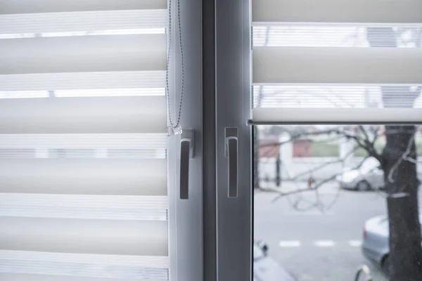 Window handle and white fabric roller blinds on the white plastic window in the living room. Close up on roll curtains indoor. — Stock Photo, Image