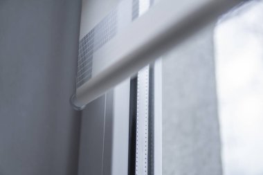 Oturma odasında beyaz plastik pencereüzerinde beyaz kumaş rulo jaluman detayları. Rulo perdeleri kapalı kapatın.