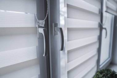 Pencere sapı ve beyaz kumaş rulo oturma odasında beyaz plastik pencereüzerinde jaluz. Rulo perdeleri kapalı kapatın.