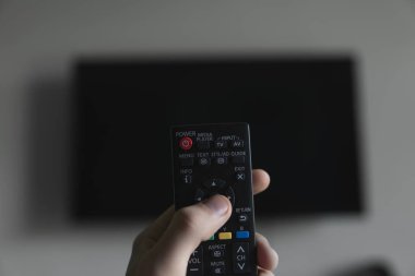 Elinde uzaktan kumanda olan adam Televizyonu açmak istiyor ve uzaktan kumandadaki düğmeye basıyor. El yakın çekimuzaktan uzaktan kumanda.