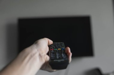 Elinde uzaktan kumanda olan adam Televizyonu açmak istiyor ve uzaktan kumandadaki düğmeye basıyor. El yakın çekimuzaktan uzaktan kumanda.