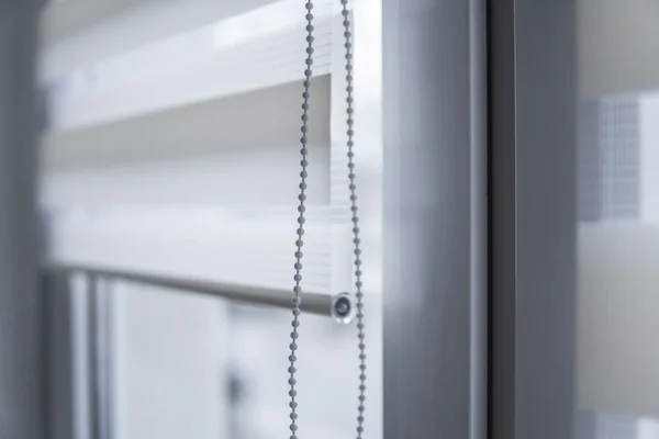 Details of white fabric roller blinds on the white plastic window in the living room. Close up on roll curtains indoor.