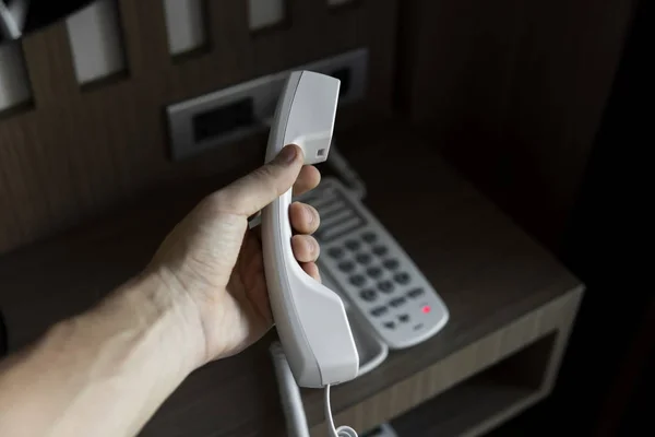 Mans hand hållande handenhet av vit Vintage telefon med grå batalomer på ett brunt bord på hotellet. — Stockfoto