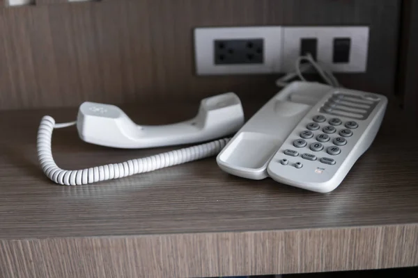 Entfernen Sie das Headset eines weißen Vintage-Telefons mit grauen Tasten auf einem braunen Tisch im Hotel. — Stockfoto