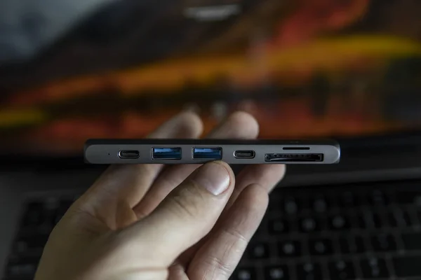 Mans hand holding The USB adapter under the Type-C connector for laptop. Multiport station for laptop with multiple different ports. USB to USB Type-C Hub Converter.