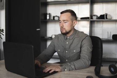 Genç işadamı ya da öğrenci bilgisayar monitörü karşı oturan bir gömlek. Düşünceli bir ifade ile ofiste bir masada bir pc üzerinde çalışıyor. Ofiste dizüstü bilgisayar üzerinde çalışan genç işadamı.