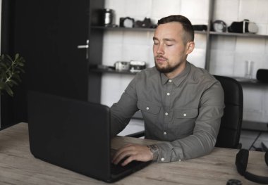 Genç işadamı ya da öğrenci bilgisayar monitörü karşı oturan bir gömlek. Düşünceli bir ifade ile ofiste bir masada bir pc üzerinde çalışıyor. Ofiste dizüstü bilgisayar üzerinde çalışan genç işadamı.