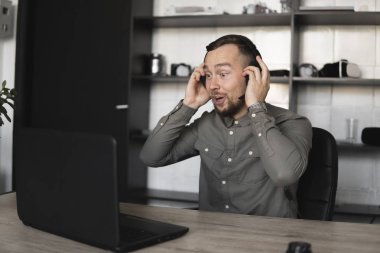 Etkilendim mutlu gülümseyen Genç işadamı ya da öğrenci bir gömlek kulaklık bilgisayar monitörü karşı oturan ve internet üzerinden biriyle konuşan. Ofisteki bir masada bir bilgisayar üzerinde çalışmak.