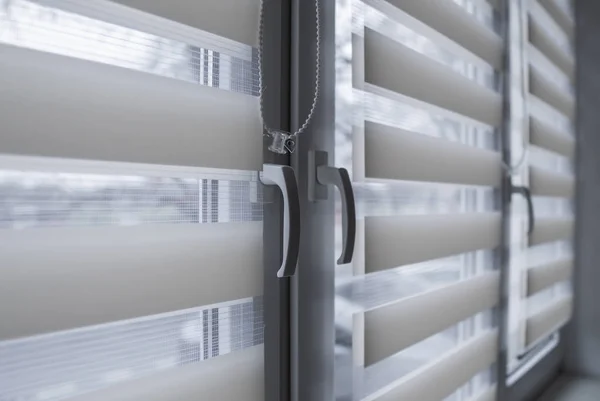 Window handle and white fabric roller blinds on the white plastic window in the living room. Close up on roll curtains indoor.